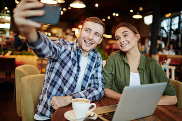 Happy young friends taking photo of themselves while gathered in lovely cafe and enjoying delicious coffee, waist-up portrait