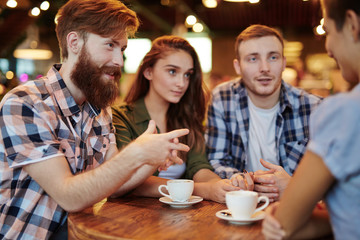 Group of creative interior designers discussing promising joint project while having coffee break in lovely small cafe, waist-up portrait