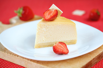 Piece of Vanilla Cheesecake with Strawberries on white plate, on bright red background.