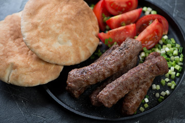 Close-up of grilled cevapi served with pita bread, sliced fresh tomatoes and onion, studio shot