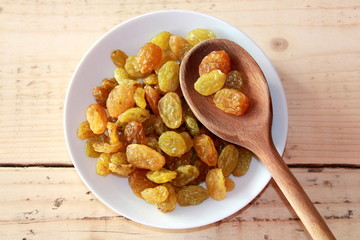 Dried Grapes on a White plate with a wooden spoon
