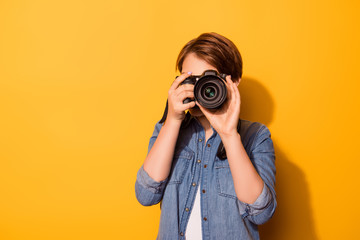Close up photo of female photographer photographing with a camera in casual clothes on the bright yellow background - obrazy, fototapety, plakaty