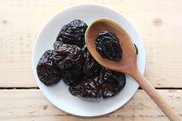 Dried plums on a White plate with a wooden spoon