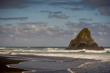 Auckland, New Zealand - March 2, 2017: Black sand Karakare Beach under blue cloudy sky with, Te...