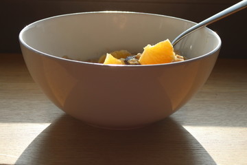 biała miska śniadaniowa z owsianką, pomarańczami i łyżką