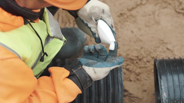 Worker squize white glue on finger in glove and apply it on edge of black plastic pipe. Slowmotion close up