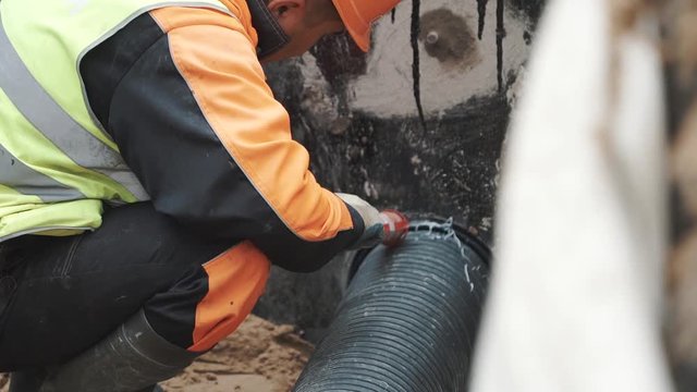 Builder applying sealant on stitch between black ribbed plastic tube and concrete hole