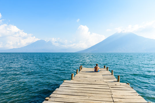 Man sitting on Pier at San Marcos La Laguna with beaufiful scenery of Lake Atitlan and volcanos - Guatemala