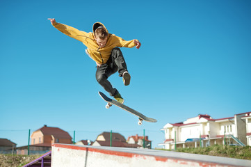 A teenager skateboarder does an flip trick in a skatepark on the outskirts of the city - obrazy, fototapety, plakaty