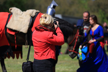 Kobieta blondynka robi zdjęcia damie i rycerzowi z koniem.