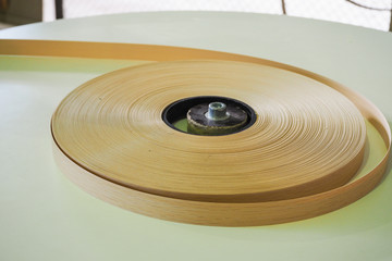 At a furniture factory edge plastic roll is fed into an edge banding machine.
