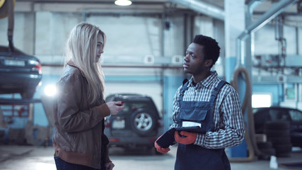 Female blond client giving keys from her car to mechanic in uniform and talking about problem