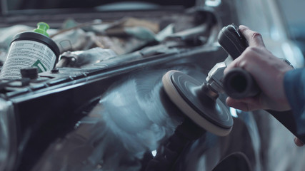 Mechanic using a rotary polisher on a the paintwork of a black car in a body shop to finish off a repair after an accident
