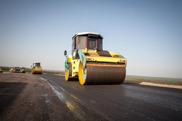 Asphalt compactor of yellow color with iron heavy compactors builds road - obrazy, fototapety, plakaty