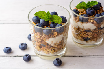 Granola with yogurt and blueberries in glass on white wooden table.