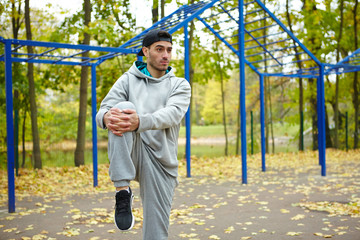 Sporty young man doing warm-up exercises while enjoying picturesque view of autumn park