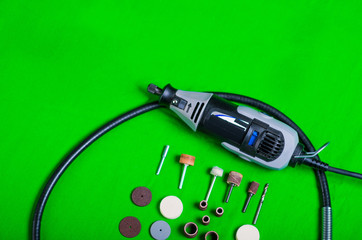 A gray drill with drilling accessories on green background aerial view