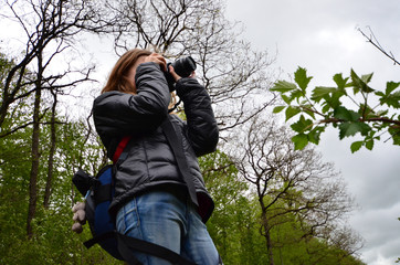 Young blond girl taking photos in the forest