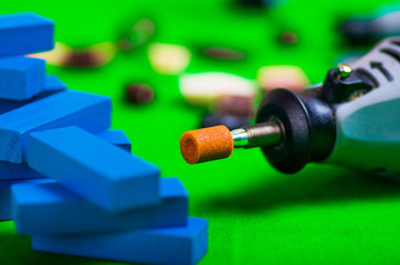 A closeup of gray drill with a small blue wooden pieces on a green background