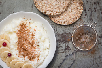 Rice porridge with fruit and berries in a white plate on rustic background. Top view.