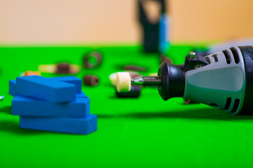 A gray drill with a small blue wooden pieces on a green background