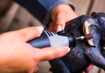 A closeup of a hardworker woman using a polisher over a wood elephant on a wooden background