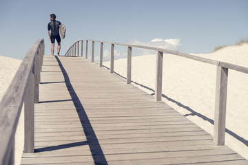 European man with surfboard looking into the distance, young male surfer on beach, summer sports background with path beach