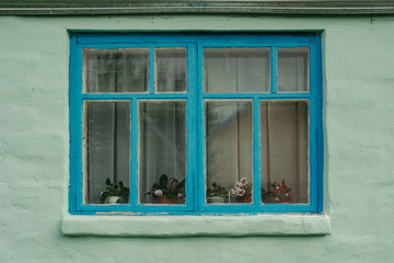 Blue wooden window of an old private house, whose walls are painted in light green color. The old building. Plastered walls.