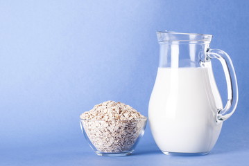 Raw oatmeal in a bowl and milk in a jar on a blue background
