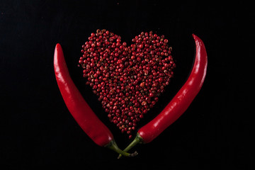 Two red chili peppers on a black background. Heart shaped peas peppers
