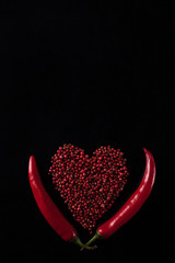 Two red chili peppers on a black background. Heart shaped peas peppers
