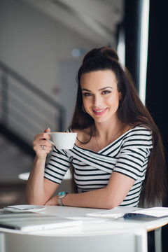 Portrait of a charming woman sitting at the table and holding a cup of tea looking at the camera.