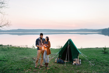 Man and woman lovers hold a flashlight at dawn near the lake