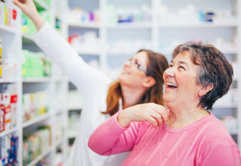 Pharmacist and senior costumer looking and searching for a medication on pharmacy shelf laughing