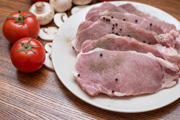 Slices of raw meat lie on a plate next to tomatoes and champignons