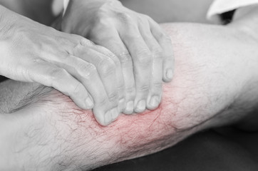 Closeup of hands of chiropractor/physiotherapist doing calf muscle massage to man patient,  in silhouette studio. Red color pain.