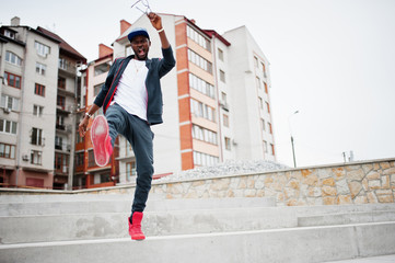 Portrait of jumping stylish african american man on sportswear, cap and glasses. Black men emotion model street fashion.