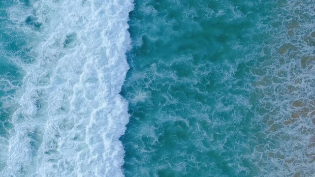 Aerial drone slow motion video of beautiful sea waves crashing on shore. Tracking shot of ocean waves creating a texture from the white sea foam