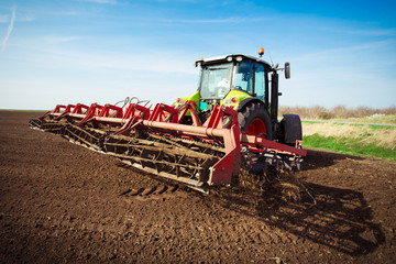 Farmer in tractor preparing land with seedbed cultivator in early spring