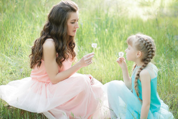 Obraz premium A family from mother and daughter is playing outdoors. Sitting on the green grass, holding dandelions in their hands