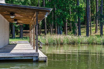 Fototapeta na wymiar Lake boat house resting on reflective lake shoreline water. Relaxing tranquil outdoor scene of woods, grass and water with boat house. 