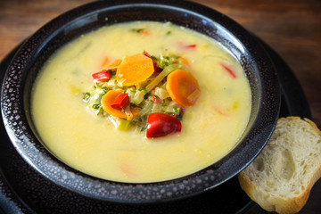 cream soup from vegetables like carrots, red peppers and leek with bread in a dark bowl on a rustic wooden table, close up