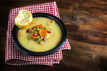  vegetable soup with carrot, red pepper,  leek and  bread in a dark bowl on a red white napkin, rustic wooden table, large copy space, selected focus, narrow depth of field