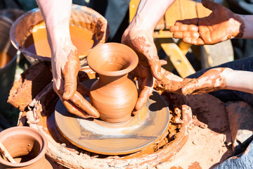 Potter's hands guiding a child hands to help him to work with the ceramic wheel. Work on the potter's wheel at the outdoors
