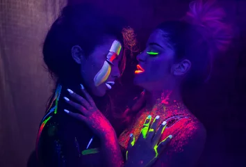 Sexy lesbische Models im UV-Neonlicht mit fluoreszierend leuchtendem Body Art Make-up. Moment vor dem Kuss. Soft-Fokus-Bild. Dunkles Low-Key-Bild. Bild mit weichem Fokus. © Igor Kardasov