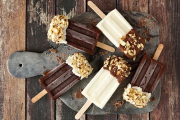 Chocolate and almond dipped white and dark popsicles, overhead view on a dark background