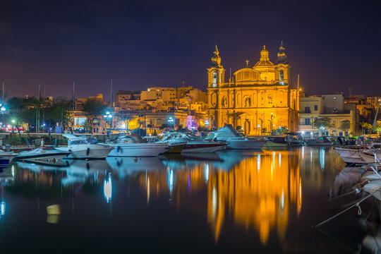 Msida, Malta - The beautiful Msida Parish Church with yachts and boats and reflection on the water by night