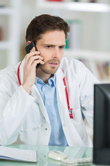 young male doctor sitting at desk and phoning