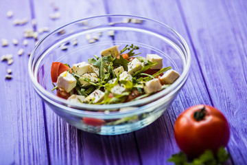 Tasty fresh salad and tomate on purple wooden table. Food