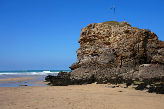 Rocky outcrop on a sandy beach with sea and surf in distance under blue sky